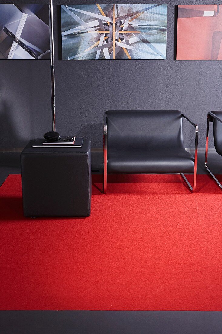 Dark grey lounge chairs, pouffe and wall enlivened by red carpet and gallery of artworks