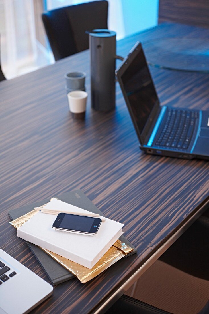 Laptop und Thermoskanne, Buch und Smartphone auf elegantem Edelholz-Schreibtisch