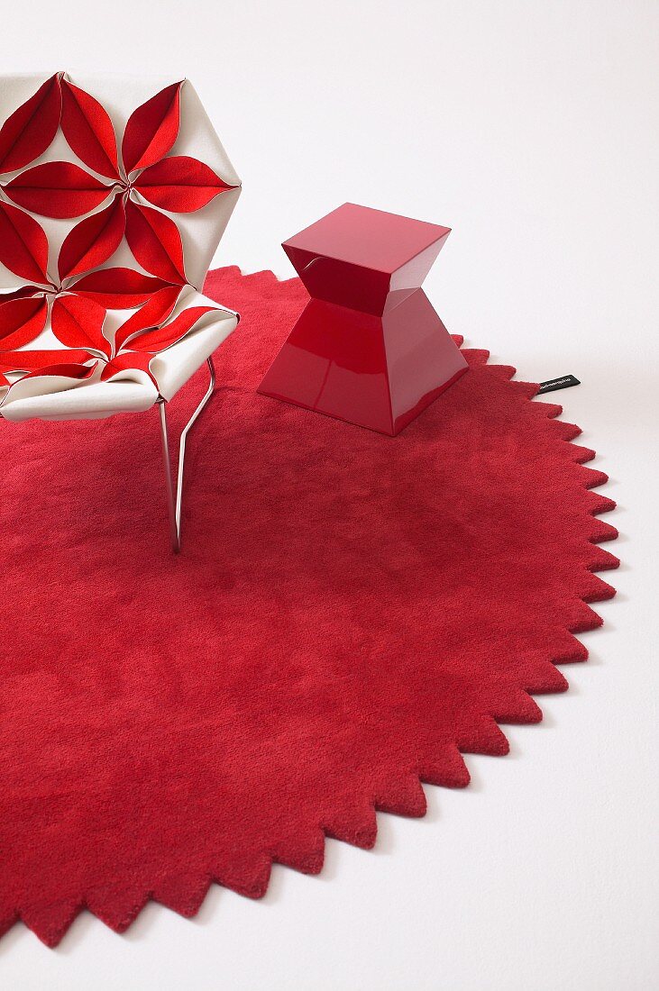 Designer Sessel mit Bezug aus dreidimensionalem Blumenmtoiv und roter Beistelltisch auf rundem Teppich mit Zackenrand