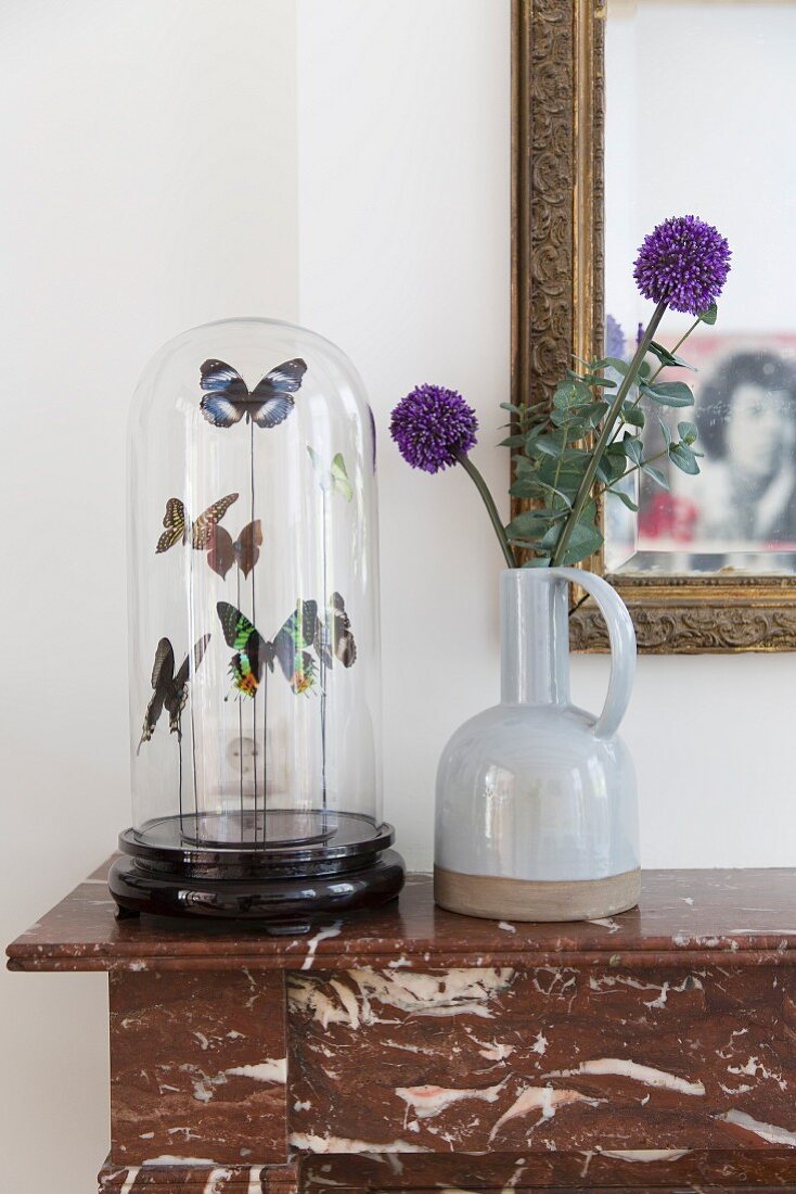 Ceramic vase and prepared butterflies under glass cover on marble mantelpiece