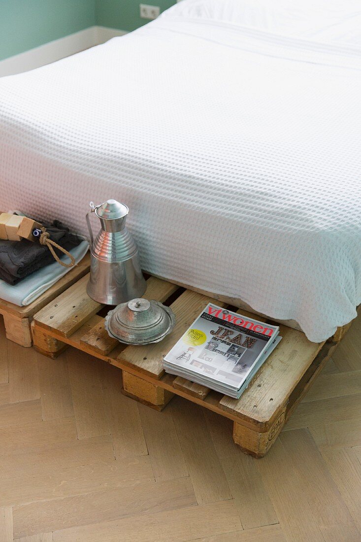 Bed with waffle piqué bedspread and protruding pallet frame used as bedside table