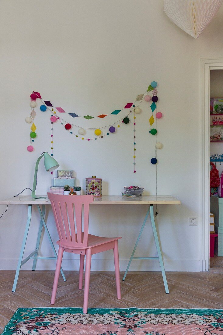 Kinderschreibtisch auf Böcken mit rosa Stuhl, bunte Ketten an der Wand und Orientteppich am Boden