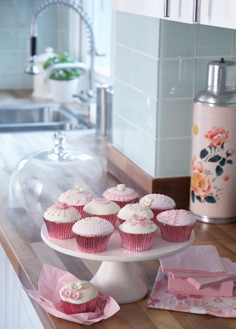 Verzierte Muffins in rosa Förmchen auf weisser Etagere