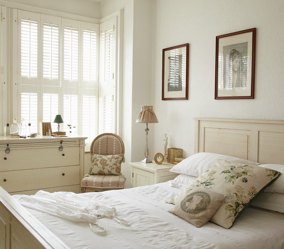 Traditionelles Schlafzimmer im Vintage Weiß mit floralen Kissen und Bilder über dem Bett