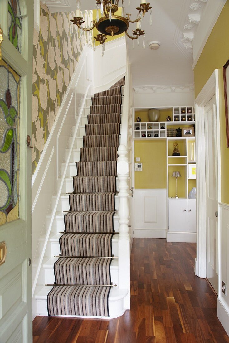 Treppenaufgang mit Teppich, grüne Wandgestaltung und weiße Holzeinbauten in der Diele