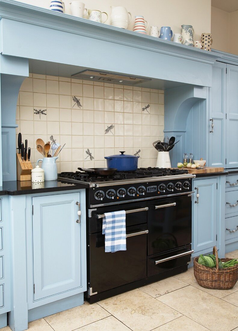 Vintage, black gas cooker under mantel hood flanked by country-house-style kitchen cabinets painted pale blue