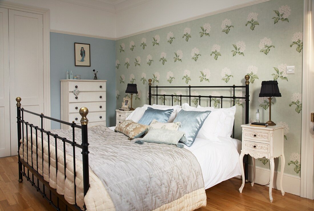 Double bed with black metal lattice frame against accent wall with floral wallpaper