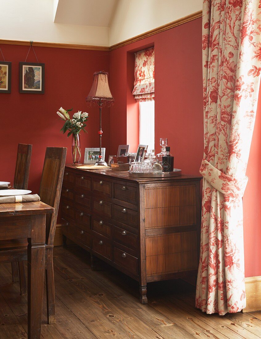 Sideboard with drawers in dining room with red-painted walls and floral curtains in English, country-house style