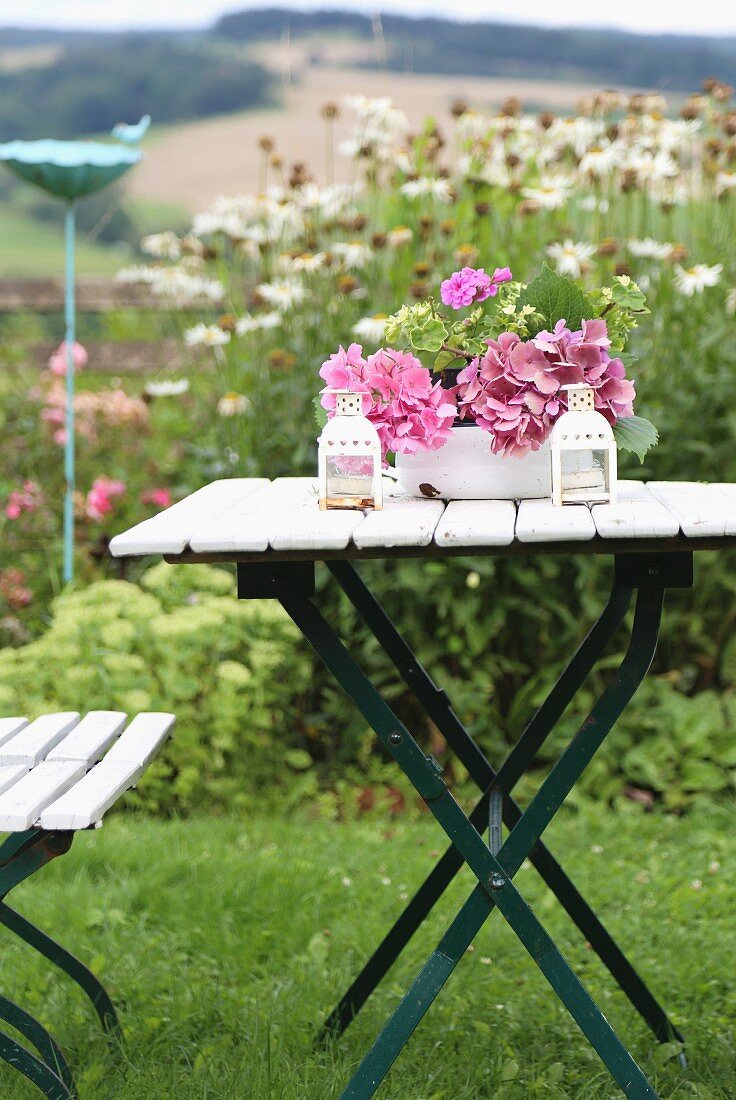 Rosa Hortensienblüten in Emailschüssel auf klappbarem Gartentisch vor Margaritenbeet
