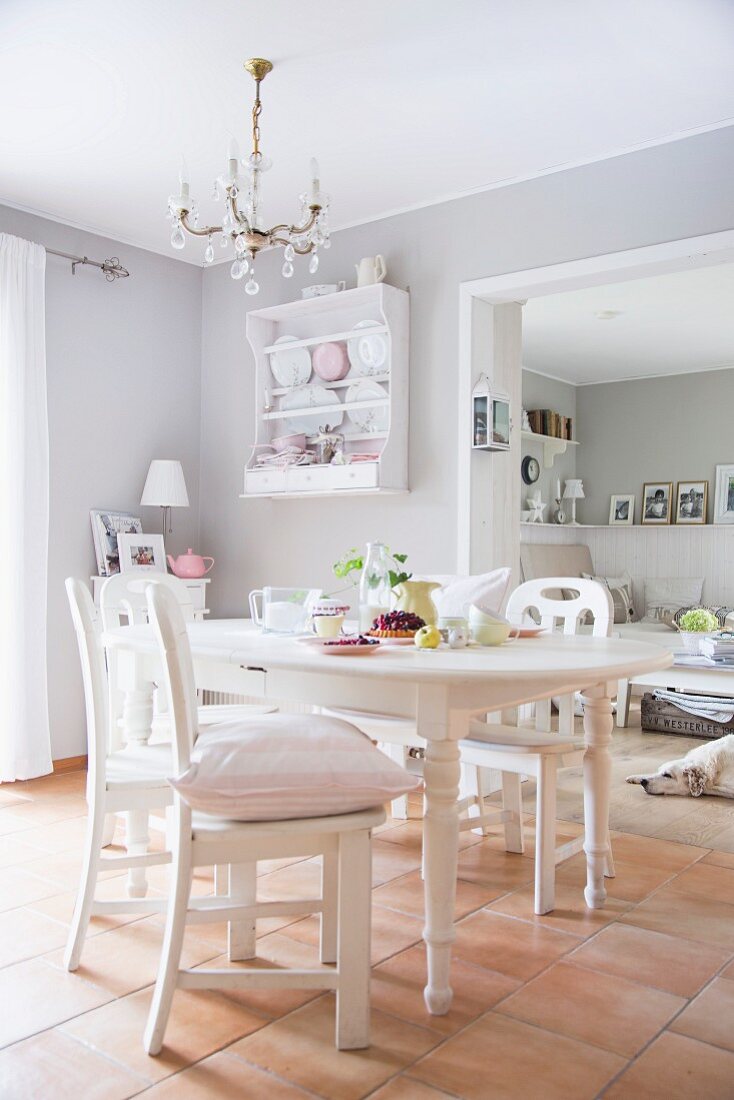 weiße Küchenstühle um Esstisch in hellgrauem Esszimmer mit Fliesenboden und Kronleuchter