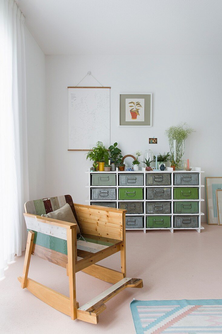 Schaukelstuhl aus farbigen Holzleisten, im Hintergrund Sideboard mit Vintage Metallkisten an Wand, in modernem Ambiente