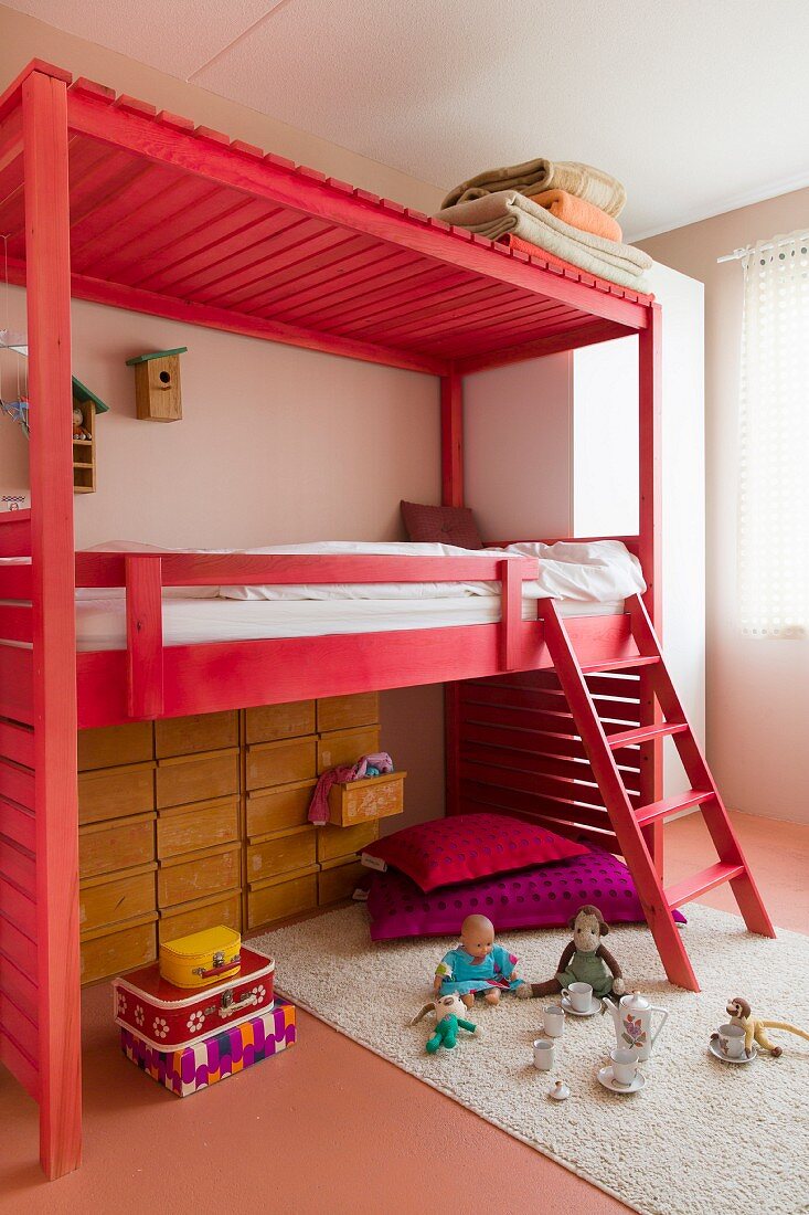 Wooden loft bed with ladder stained light red and toys on rug in child's bedroom