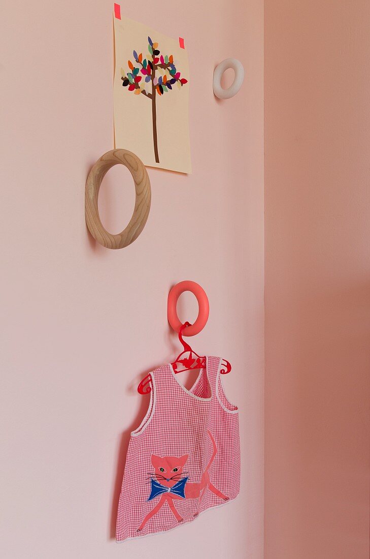 Ringförmige Halterungen mit verschiedenen Oberflächen an Wand montiert, auf Kleiderbügel gemustertes Kinderhemd