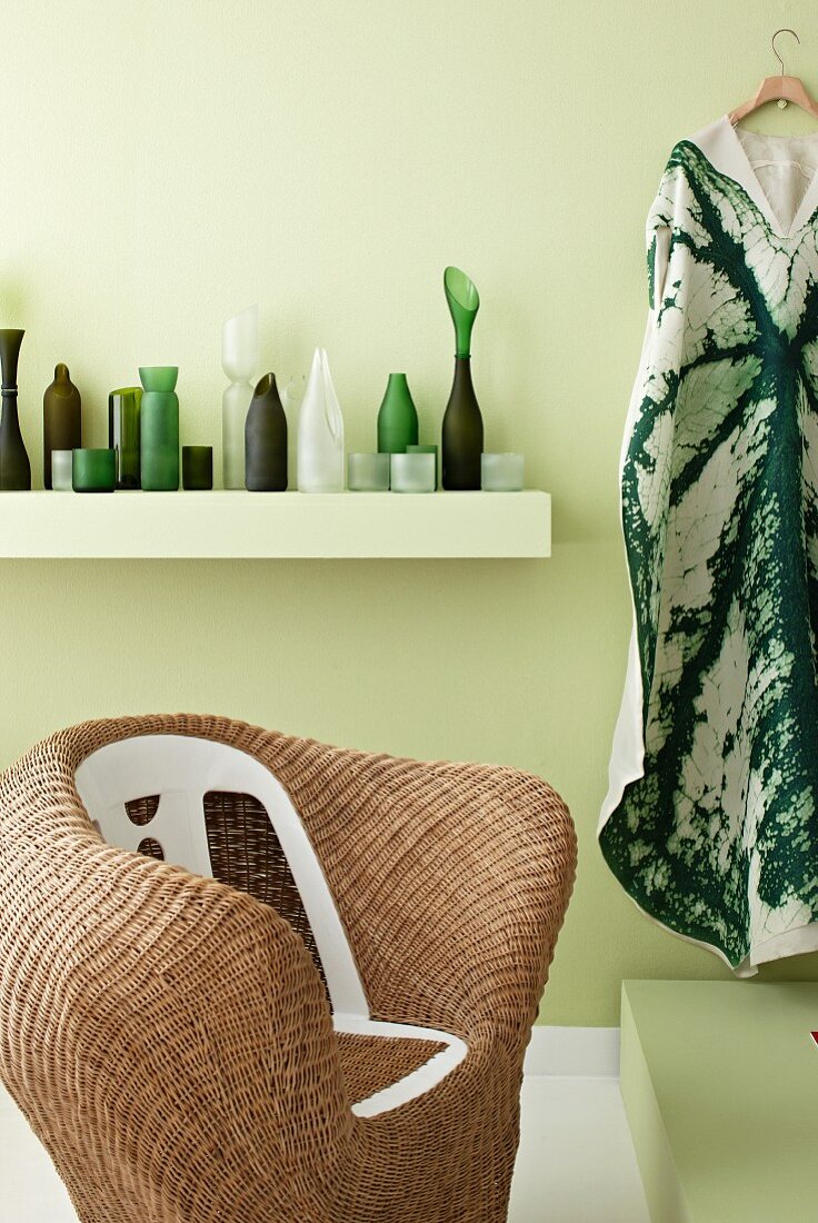 Rattan armchair in front of collection of green and white vases on white floating shelf