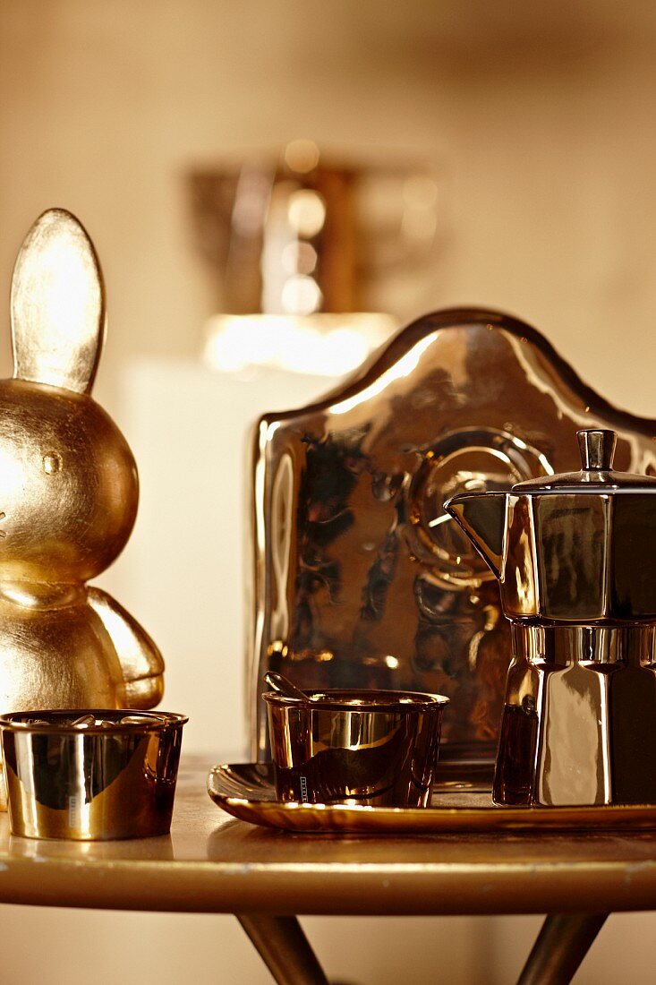 Verchromte Espressokanne und Schale neben vergoldetem Hasen auf Beistelltisch