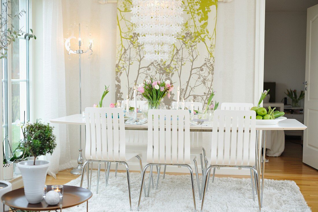 Stühle mit weisser, geschlitzter Sitzschale vor Esstisch mit Tulpenstrauss, Wandbehang mit Blumenmotiv