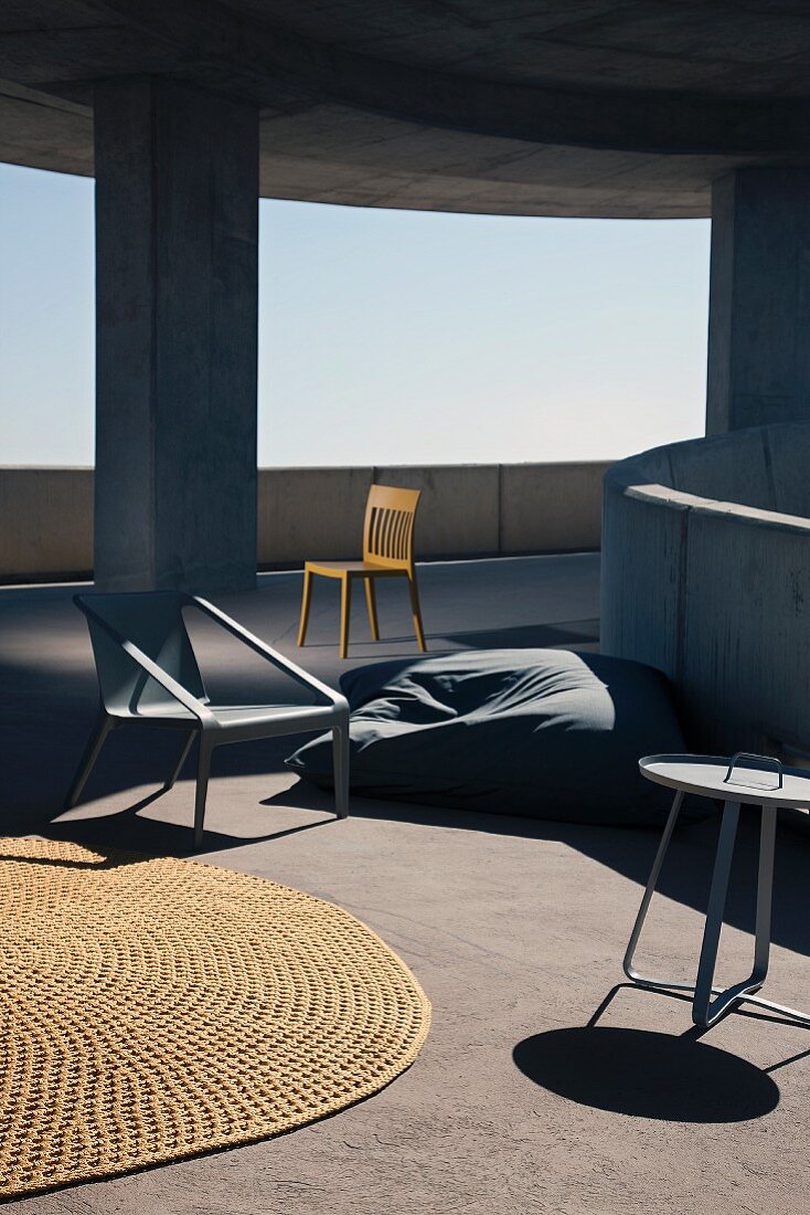 Outdoor furnishings; sisal rug, bean bag and chairs on sunny ramp of concrete building