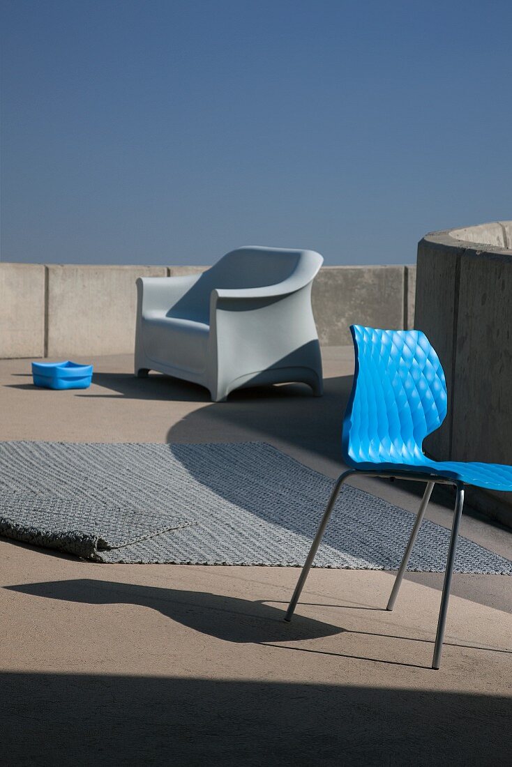 Modernes Outdoor Ensemble - Stuhl mit blauer Sitzschale, Gewebeteppich und Kunstoffsessel im Hintergrund