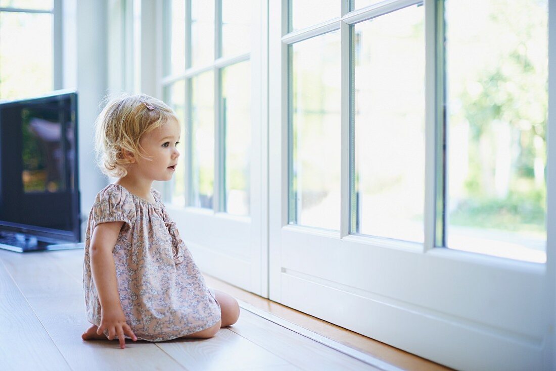 Little girl sitting on floor looking through French windows