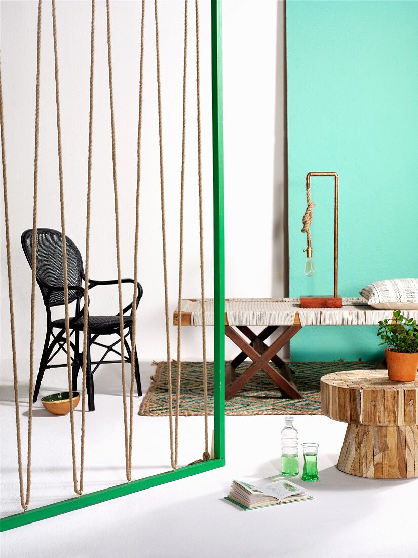 Grüner Holzrahmen mit gespannten Seilen als Raumteiler und bespannte Bank mit Leuchte aus Kupferrohr und dickem Seil