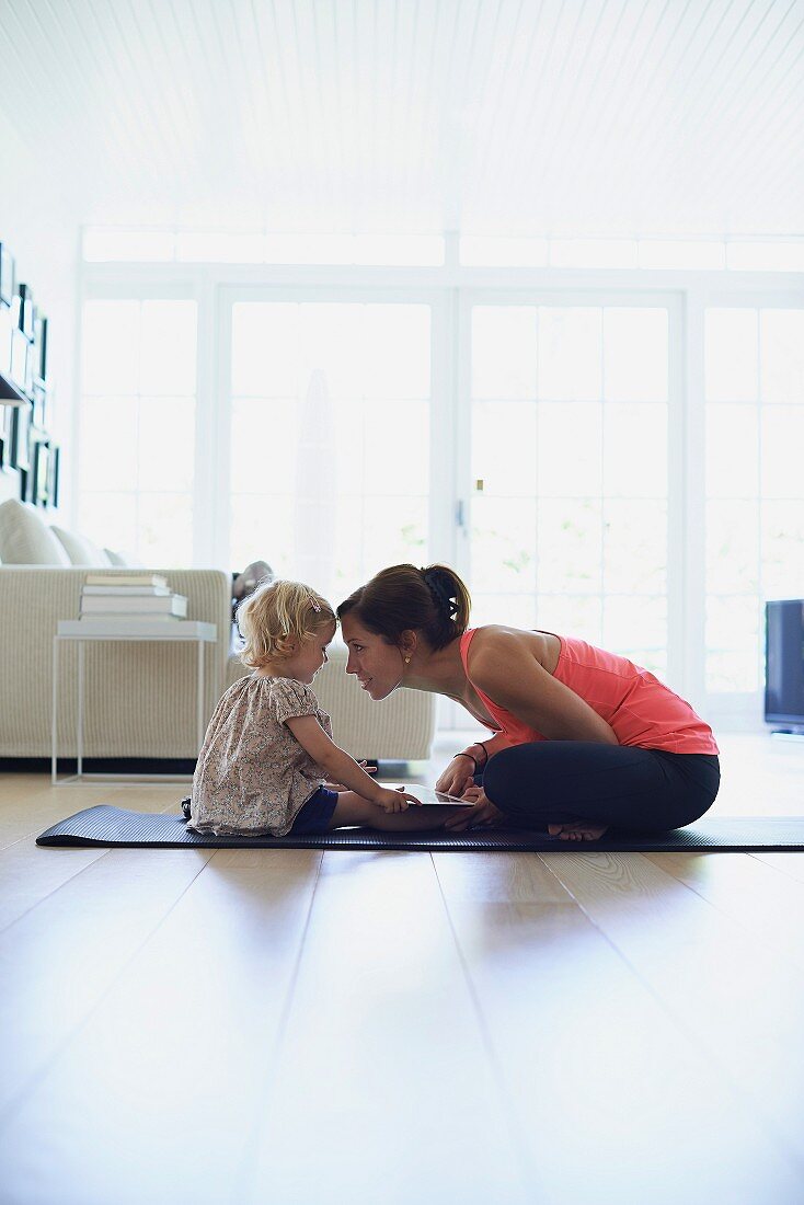 Mutter mit Tochter auf Gymnastikmatte im Wohnzimmer