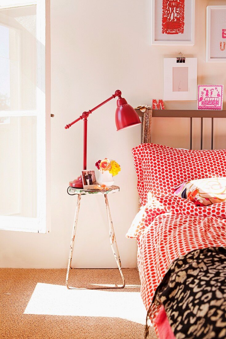 Vintage Hocker und rot lackierte Retroleuchte, daneben Bett mit gepunkteter Bettwäsche