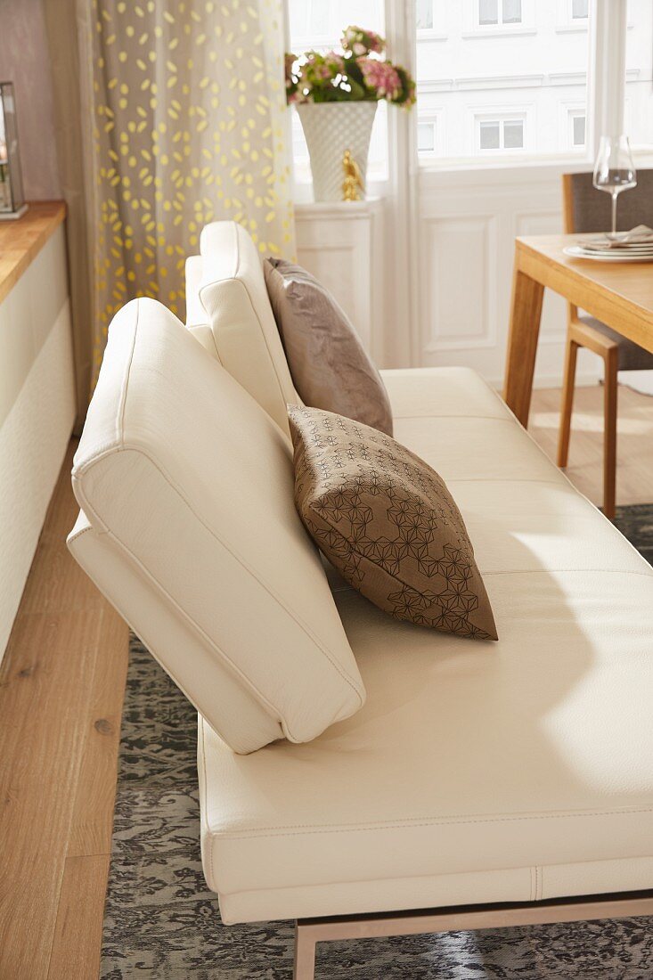 A modern, white leather bench with an adjustable backrest at a dining table