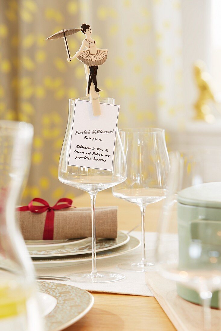 A tightrope walker figure on a clothes peg holding a menu to a wine glass