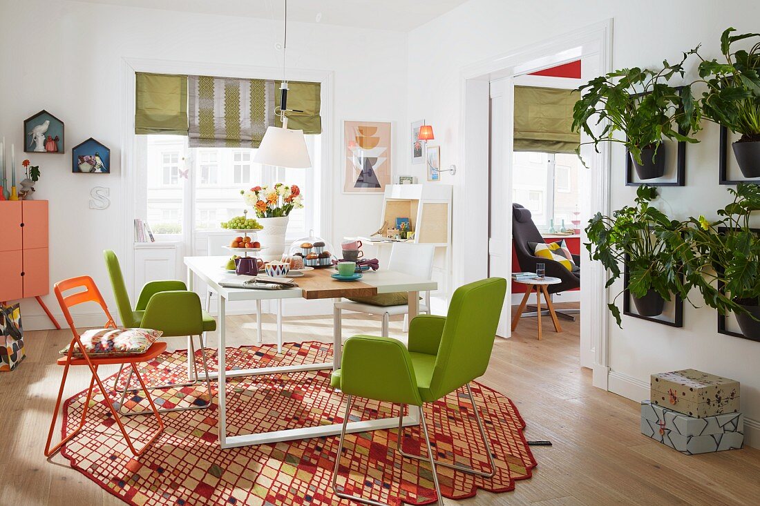 Freundlich möbliertes Esszimmer, grün gepolsterte Stühle und Klappstuhl um weissen Tisch auf Designer Teppich, an Wand Hänge-Blumentöpfe