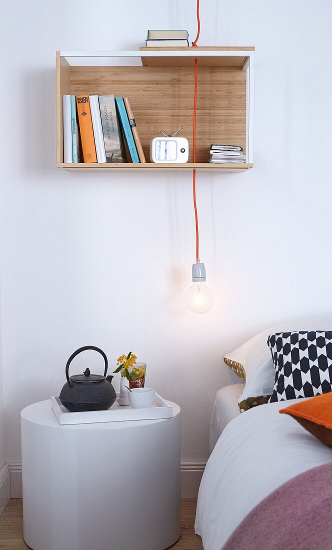 Weisser, zylindrischer Nachttisch mit Frühstückstablett neben Bett, darüber Pendelleuchte mit Glühbirne, an Wand kleines Regal