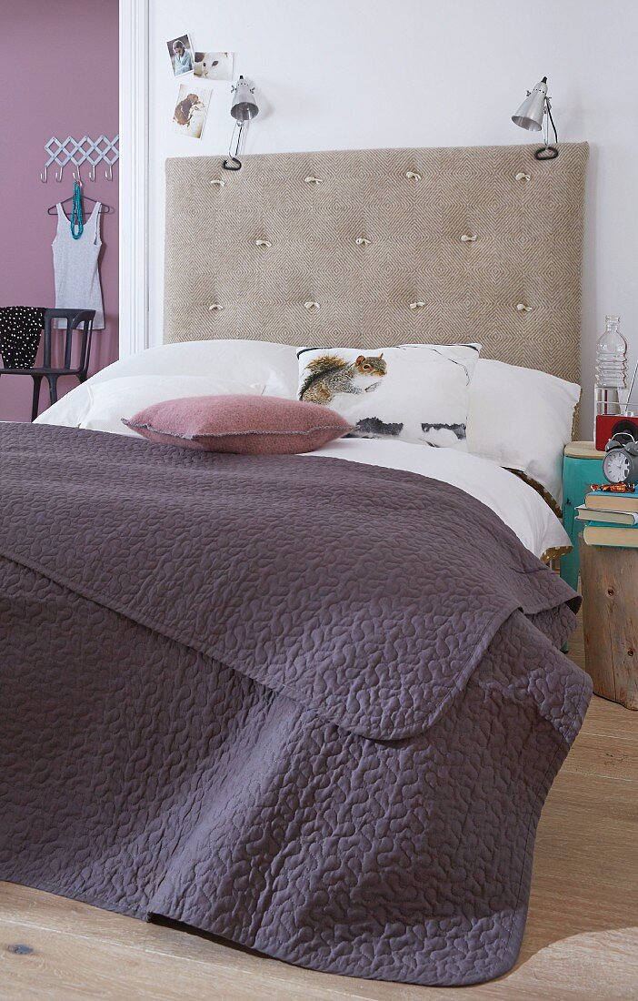 A bedspread on double bed with a homemade headboard with lamps attached to it