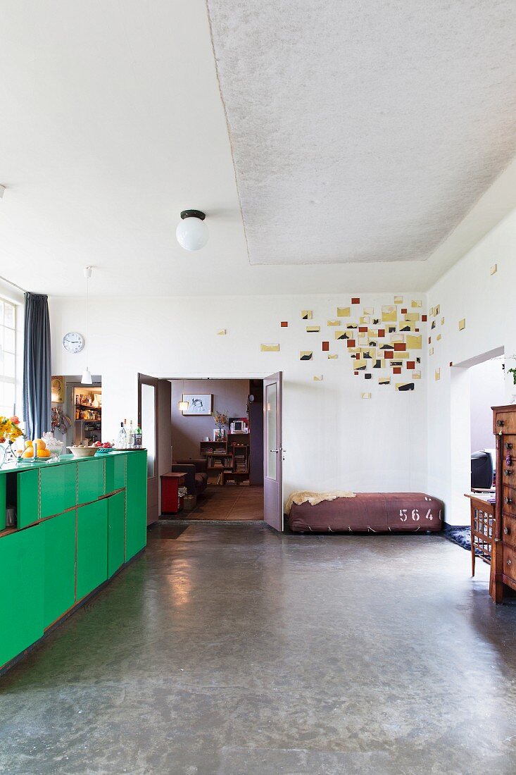 Kunstwerk in der Ecke eines Loftraums, Akustikfilz an der Decke und alter Laborschrank mit grünen Fronten vor der Küchenzeile