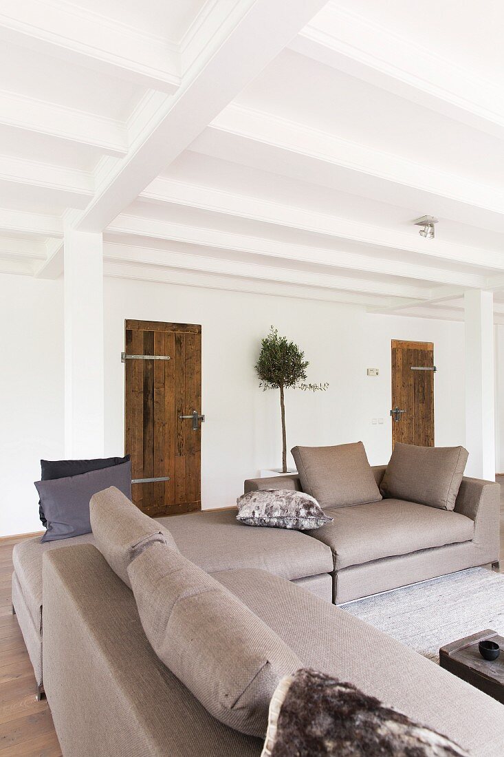 Elegante Sofakombination in Hellgrau, in offenem Wohnraum mit ländlichem Charme, weiße Holzbalkendecke