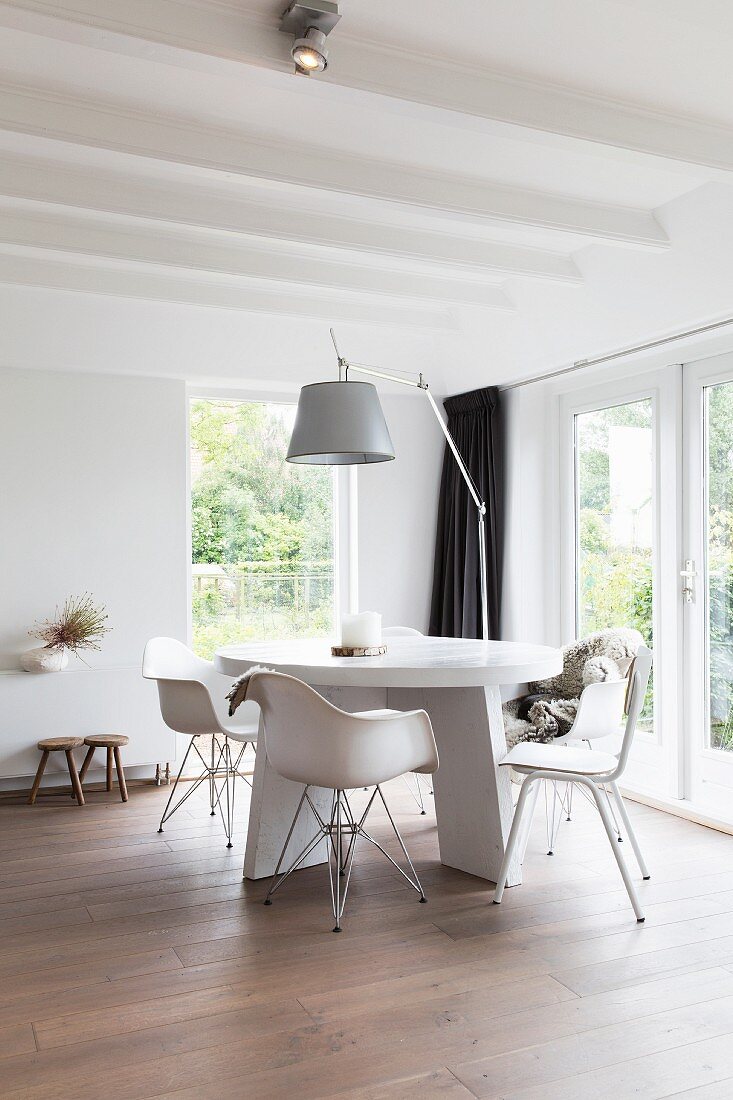 Klassiker Armlehnstühle an rundem, weißem Tisch und Bogenleuchte in moderner Wohnzimmerecke mit weisser Holzbalkendecke