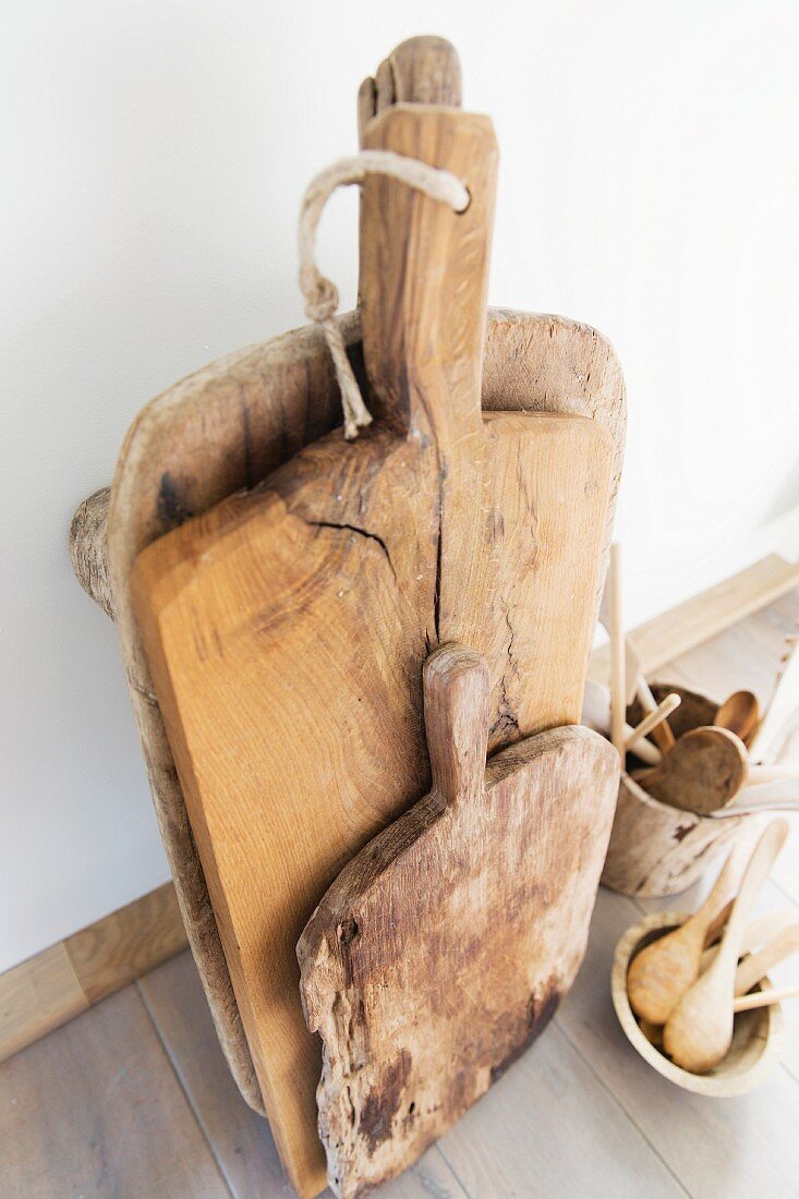 Old wooden chopping boards and kitchen utensils in wooden containers on floor