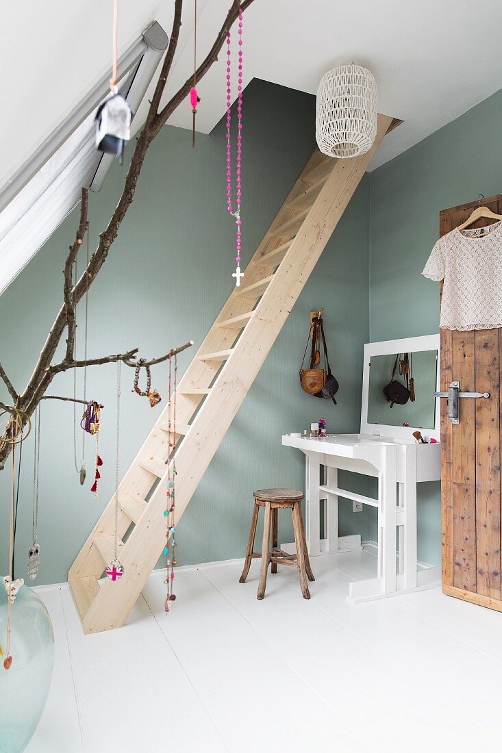 Feminine attic room with wooden ladder and white dressing table against pastel green wall
