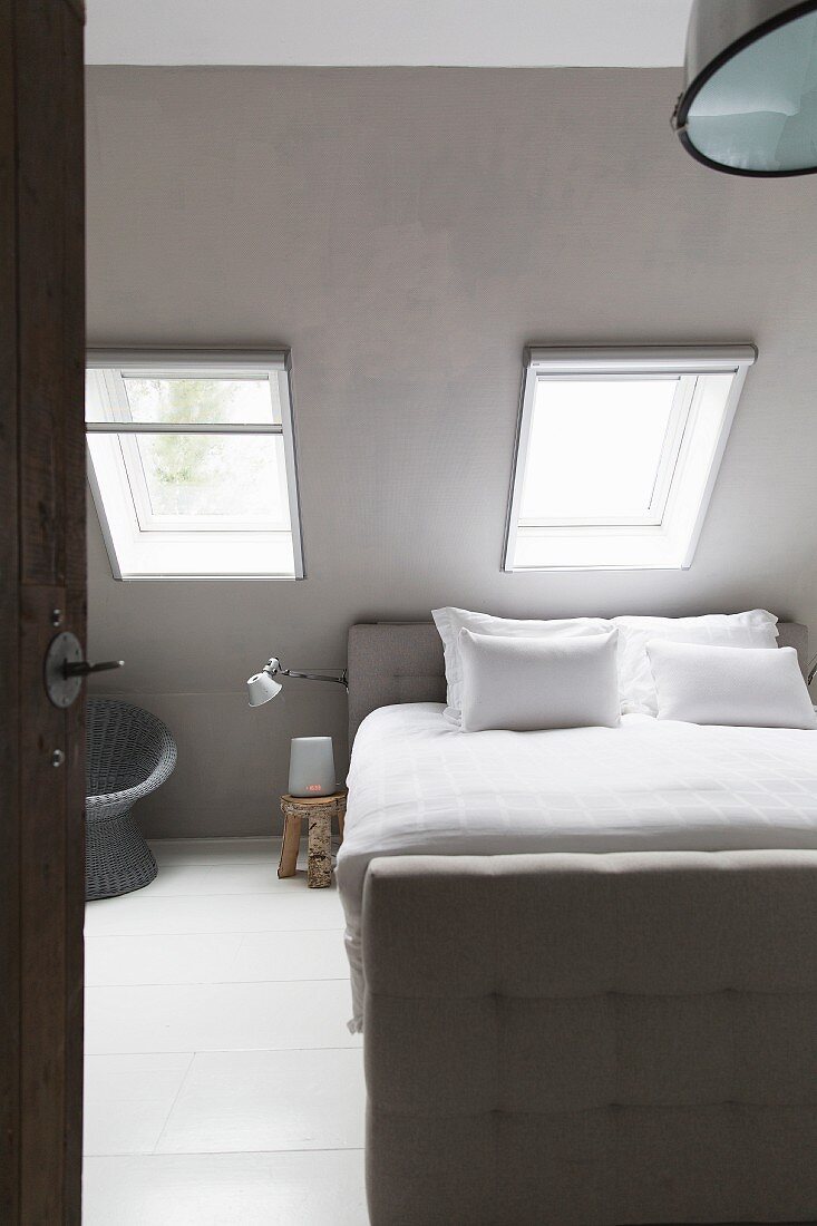 Bed with button-tufted frame below skylights in sloping ceiling