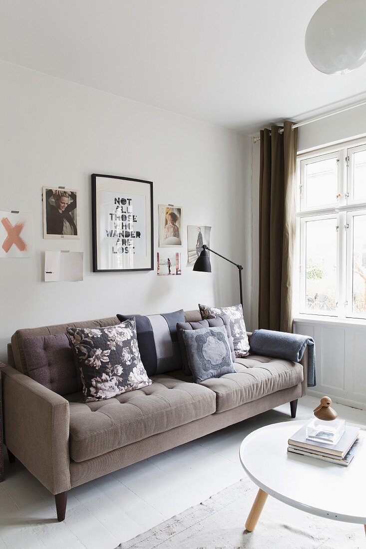 Beigefarbenes Retro Sofa mit verschieden gemusterten Kissen vor Wand mit unterschiedlichen Bildern