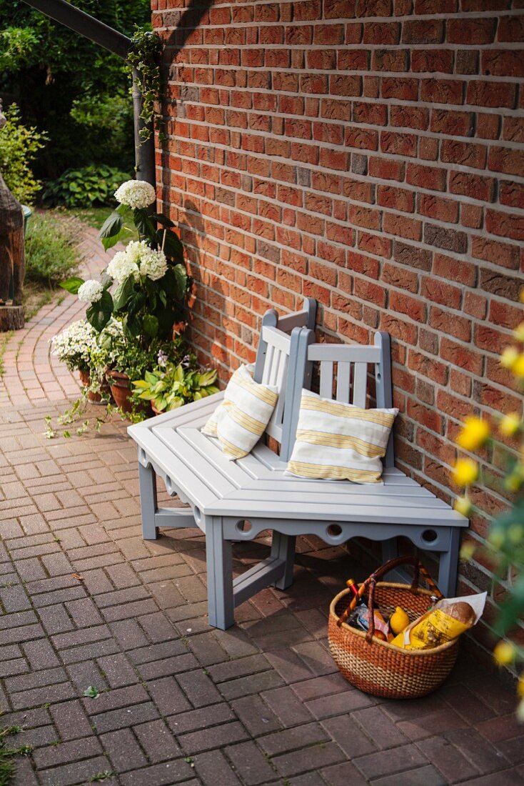 DIY wooden bench painted pale grey and white against brick wall