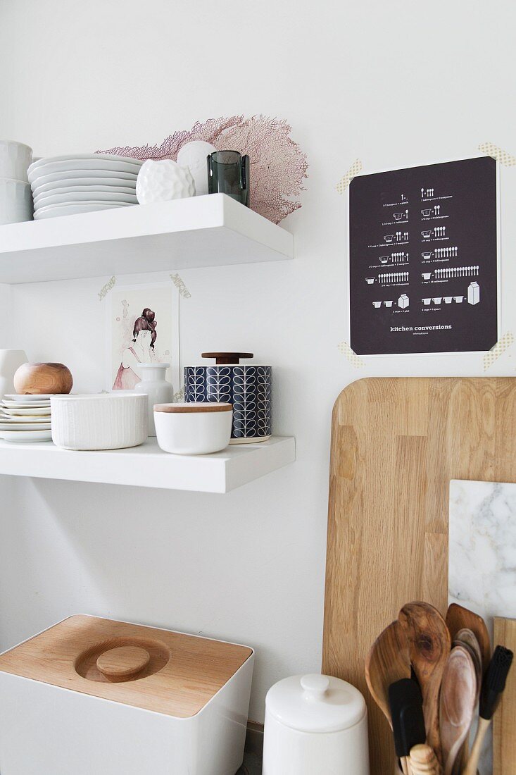 Geschirrstapel auf weissen Wandboards, darunter Brotbehälter und Küchenutensilien