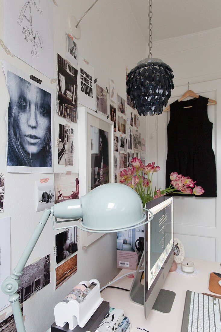 Schreibtisch mit Flachbildschirm und Retro Tischleuchte vor Wand mit Fotocollage