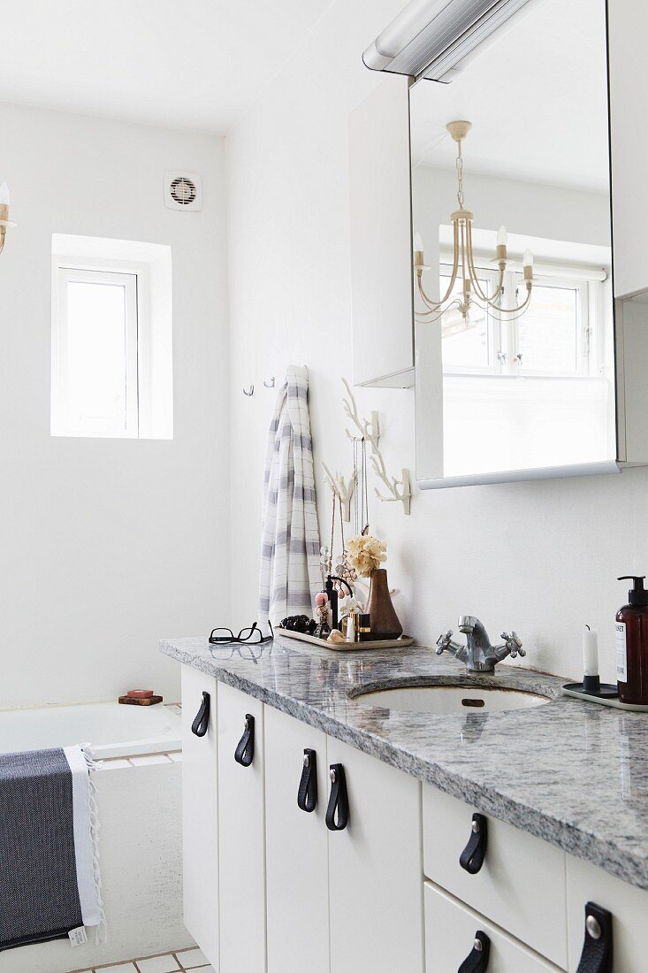 Steinplatte auf Waschtisch mit weissen Unterschränken und Ledergriffen, Spiegelschrank und Kronleuchter in weißem Bad
