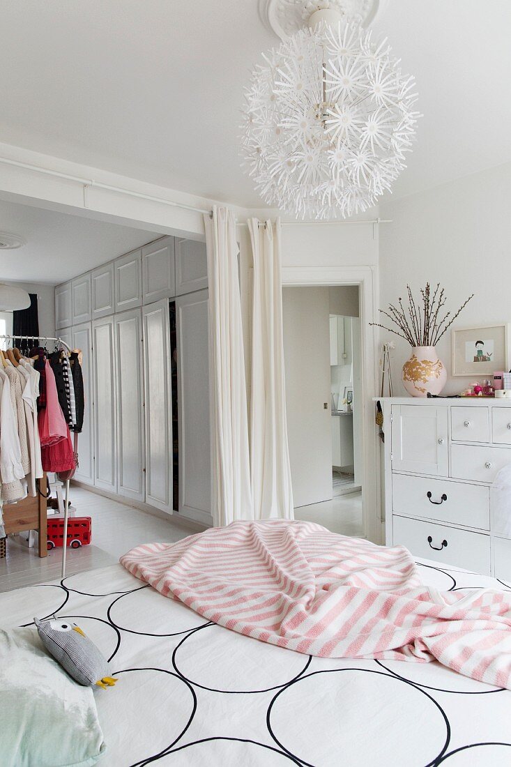 Grafisch gemusterte Bettwäsche und rosafarbene Tagesdecke auf femininem Bett mit kugelförmiger Pendelleuchte im Schlafzimmer