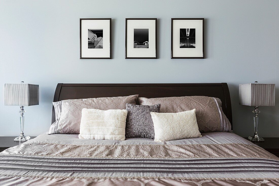 Modernes Schlafzimmer in blauen und silbernen Farbtönen; über dem Bett drei Bilder in Schwarz-weiss