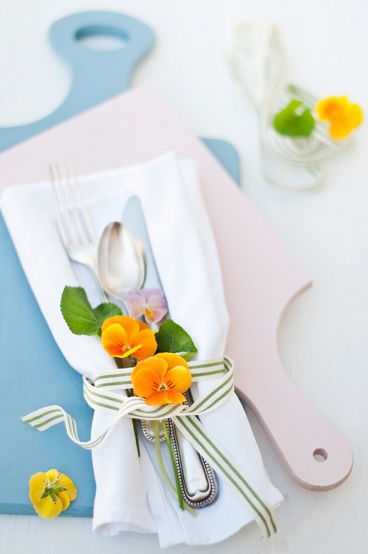Gelbe und violette Hornveilchenblüten als Tischdeko mit Besteck auf weisser Stoffserviette