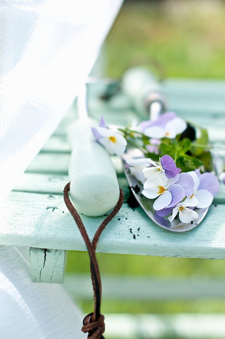 Gartenschaufel mit Hornveilchenblüten auf Gartenstuhl