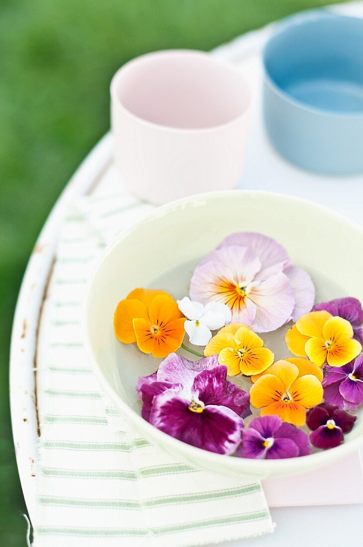 Schwimmende Hornveilchen- und Stiefmütterchenblüten in einer Schüssel auf Gartentisch
