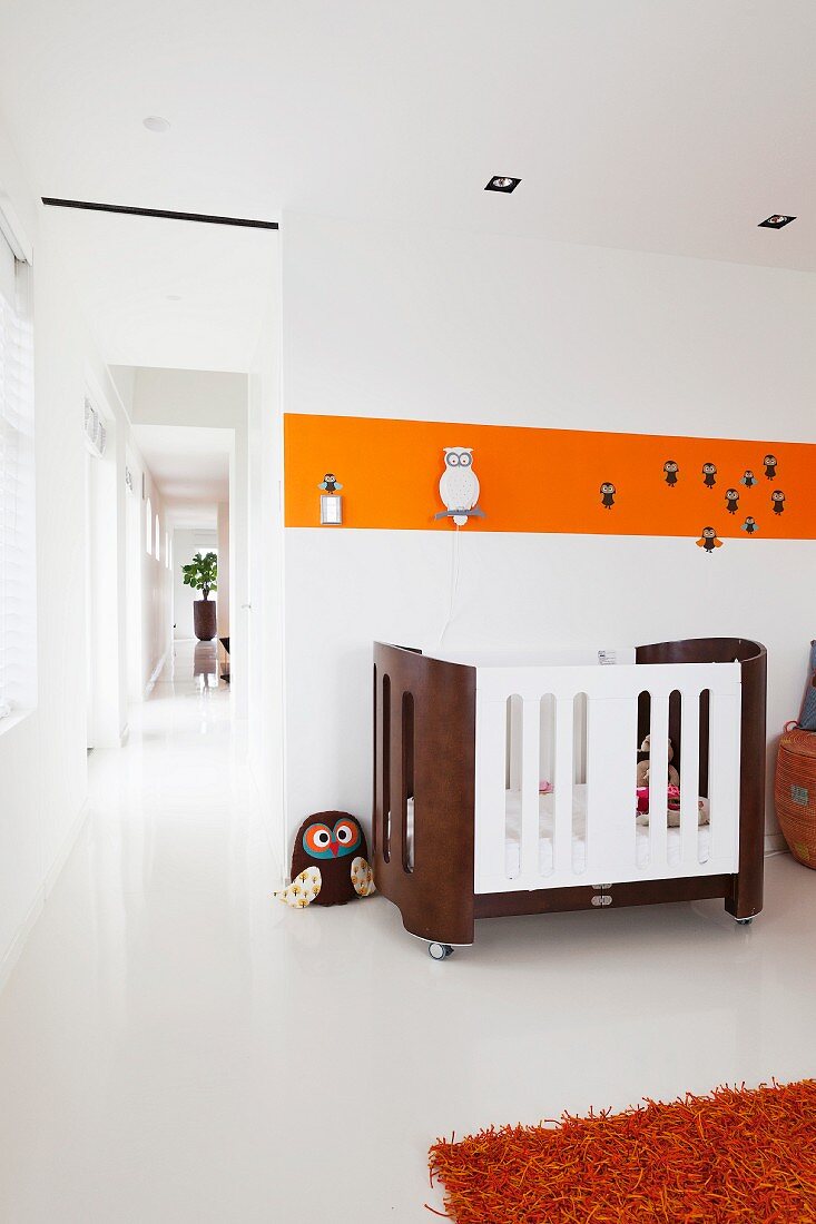 Gitterbett vor Wand mit orangem Farbstreifen im Kinderzimmer, seitlich offener Durchgang und Blick in Gang