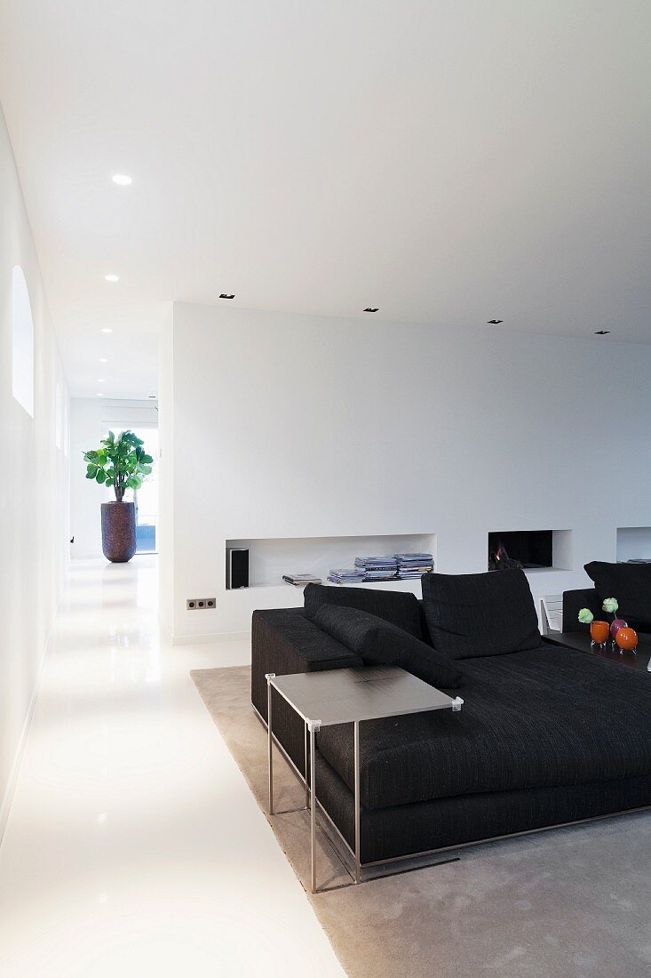 Filigraner Beistelltisch neben schwarzem Sofa, gegenüber Wand mit Regalöffnungen in modernem Wohnraum