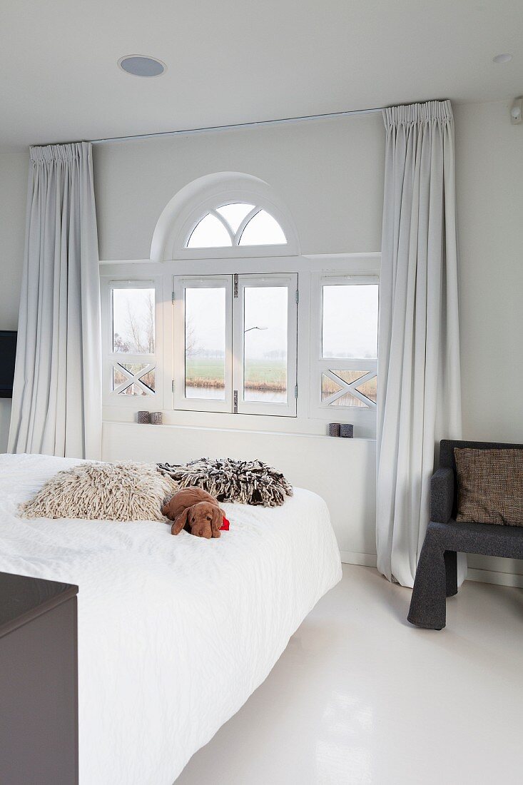 Fellkissen auf Bett, gegenüber Fenster mit halbkreisförmigem Oberlicht im Schlafzimmer